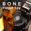 A close-up of a black fidget toy with a skull design mounted on a device.