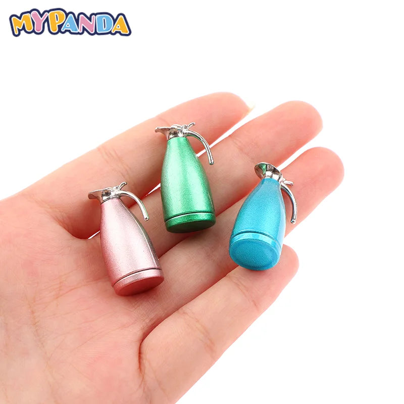 A hand holds a miniature alloy kettle in pink and green colors for dollhouse kitchen decor.