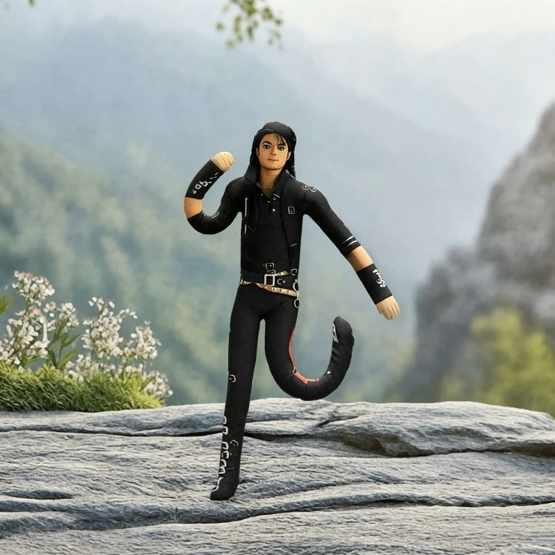Figurine en peluche noire et souple représentant un personnage sur une surface rocheuse extérieure avec des montagnes vertes 