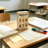 A wooden tarot card deck stands on a table next to an open notebook and a yellow note.