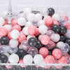 A white plastic basket filled with a variety of colorful clear and opaque play balls in pink, white, and black.