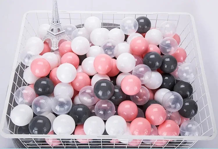 A white plastic basket filled with a variety of colorful clear and opaque play balls in pink, white, and black.