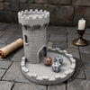 A gray medieval castle dice tower with a tray for tabletop games set on a stone surface.