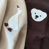 A beige knitted baby long sleeve top and pants set featuring embroidered white duck and bear cartoon designs.