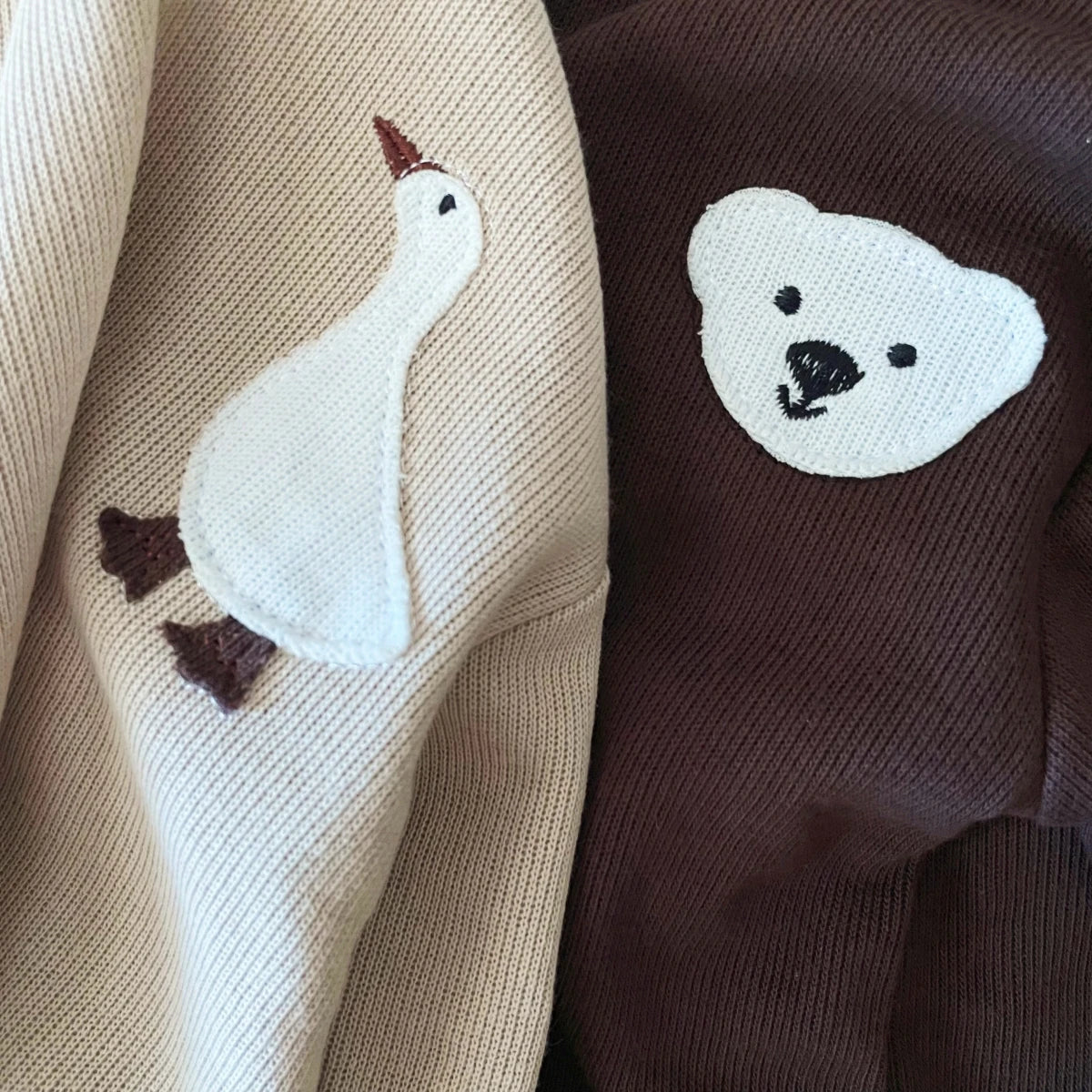 A beige knitted baby long sleeve top and pants set featuring embroidered white duck and bear cartoon designs.