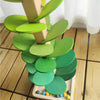 A wooden sensory music tree structure with green leaves and a marble run, set on a wooden floor.