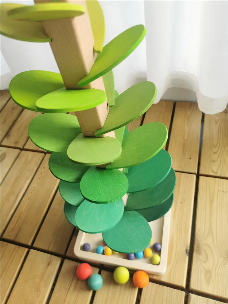 A wooden sensory music tree structure with green leaves and a marble run, set on a wooden floor.