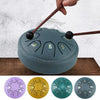 A portable steel tongue drum is shown with four color variations: purple, yellow, teal, and gray.