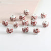 A set of twenty round ceramic flower beads in red and white patterns scattered on a white surface.