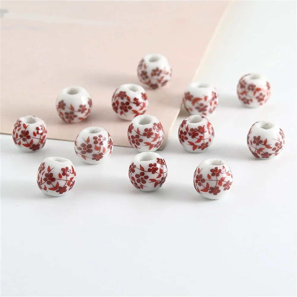 A set of twenty round ceramic flower beads in red and white patterns scattered on a white surface.