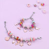 A silver charm bracelet and necklace making kit with various pink, purple, and gold charms scattered on a light purple backgr