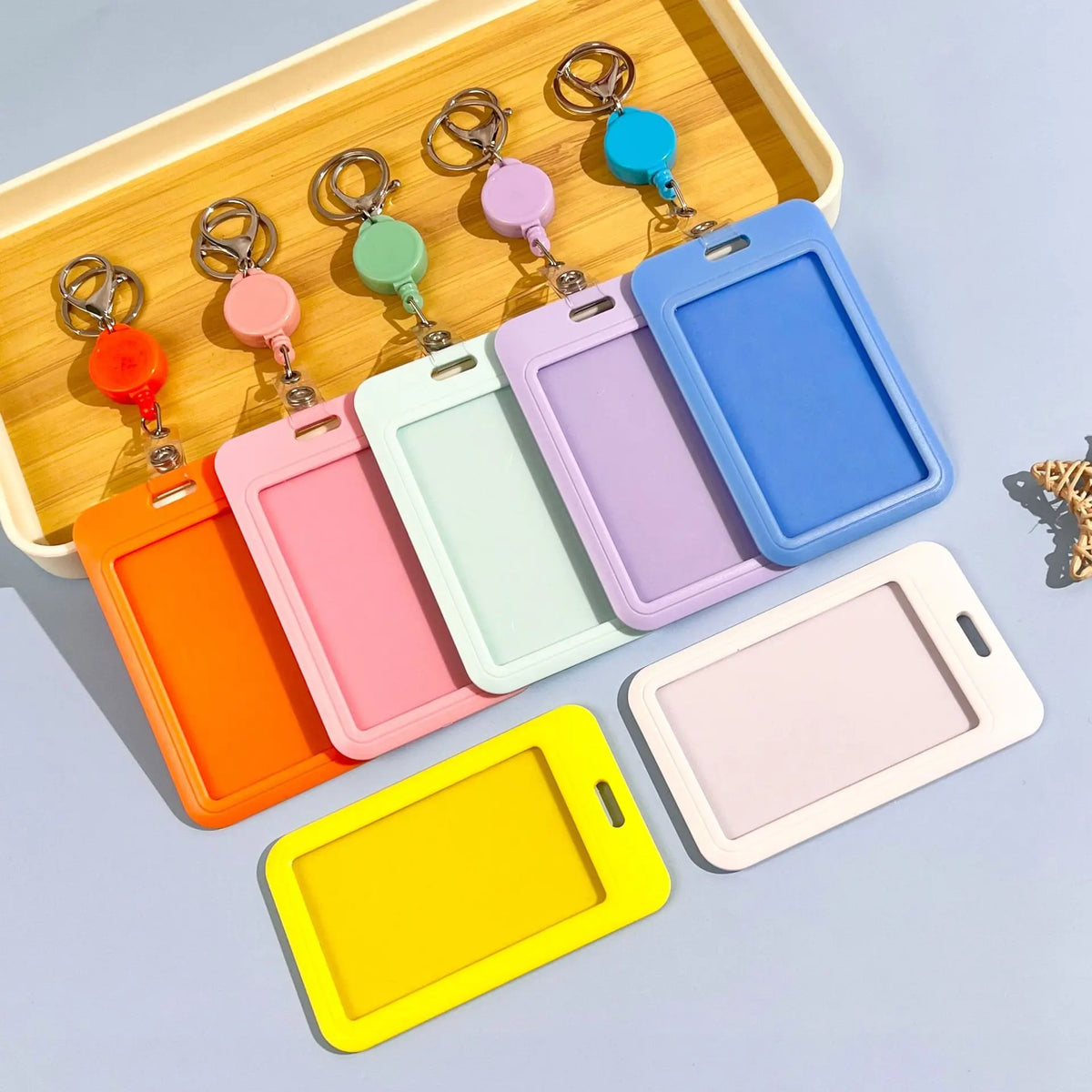 A collection of colorful retractable ID badge holders with keychains arranged in a wooden tray.