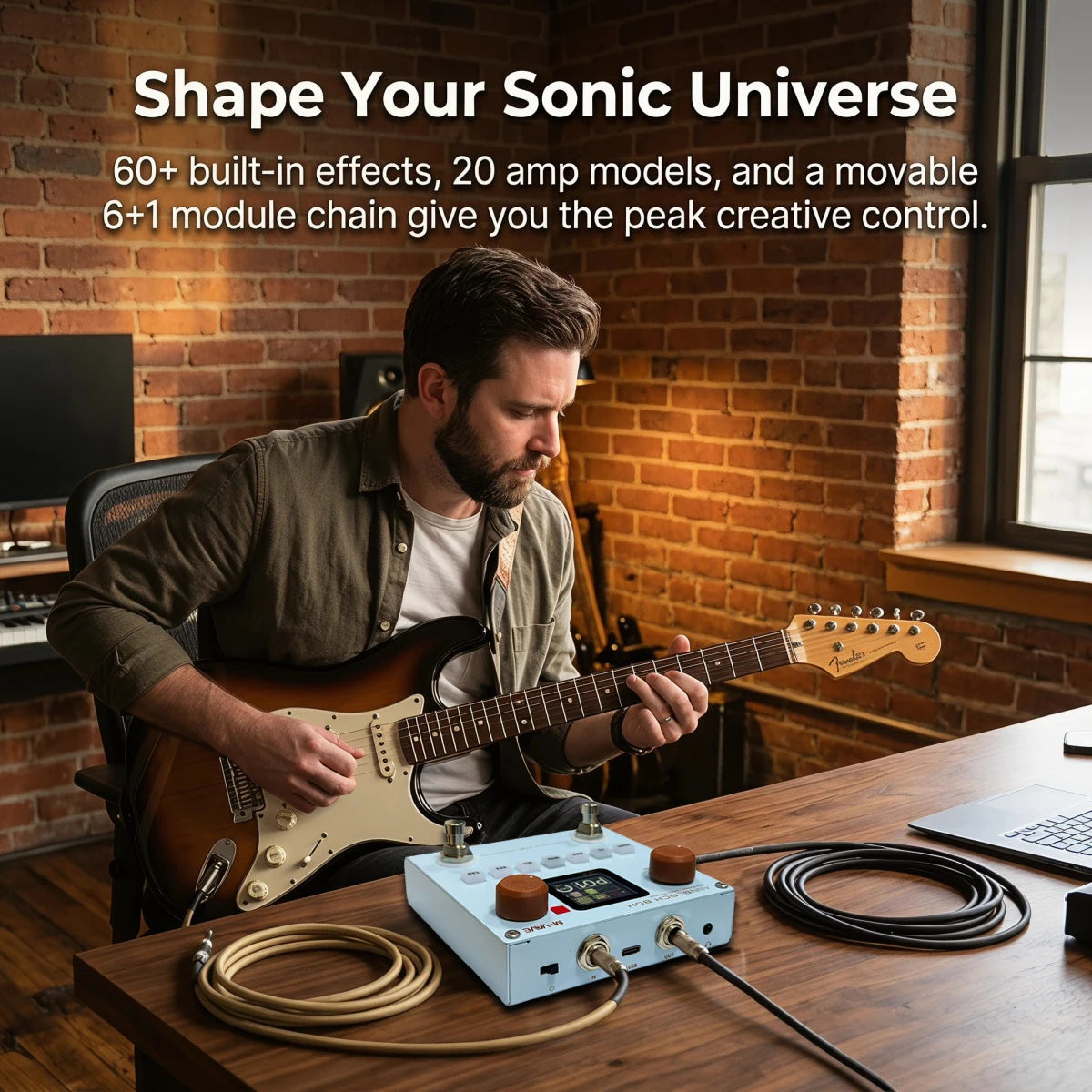 A man plays a guitar in front of a wooden desk with a portable multi-effects processor and cables.