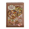 A brown notebook titled Material Book featuring illustrations of miniature scene stickers and a 3D cabin scene.