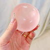 A hand holds a clear pink squishy stress relief toy shaped like a large bubble.