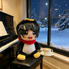 A black and white penguin plush toy with yellow accents sitting on a black surface in front of a snowy window.