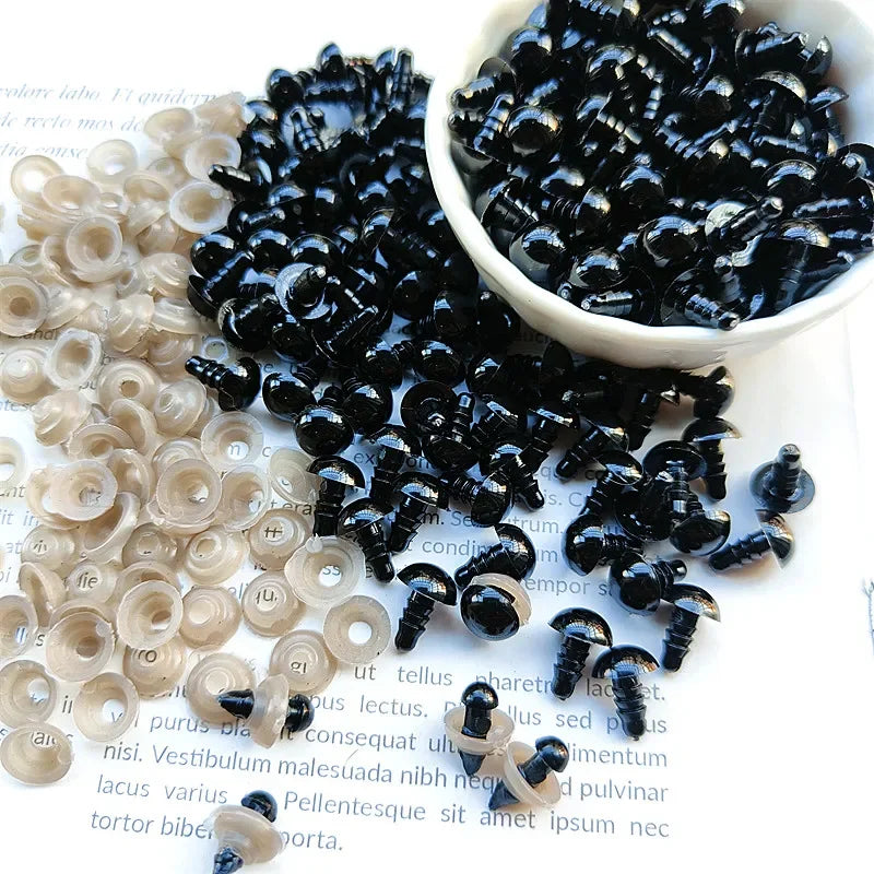 A bowl of small black plastic safety eyes for crafting, alongside a pile of clear eyes.
