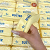 A hand holds a block of yellow butter squishy stress relief toy packaged in clear plastic.
