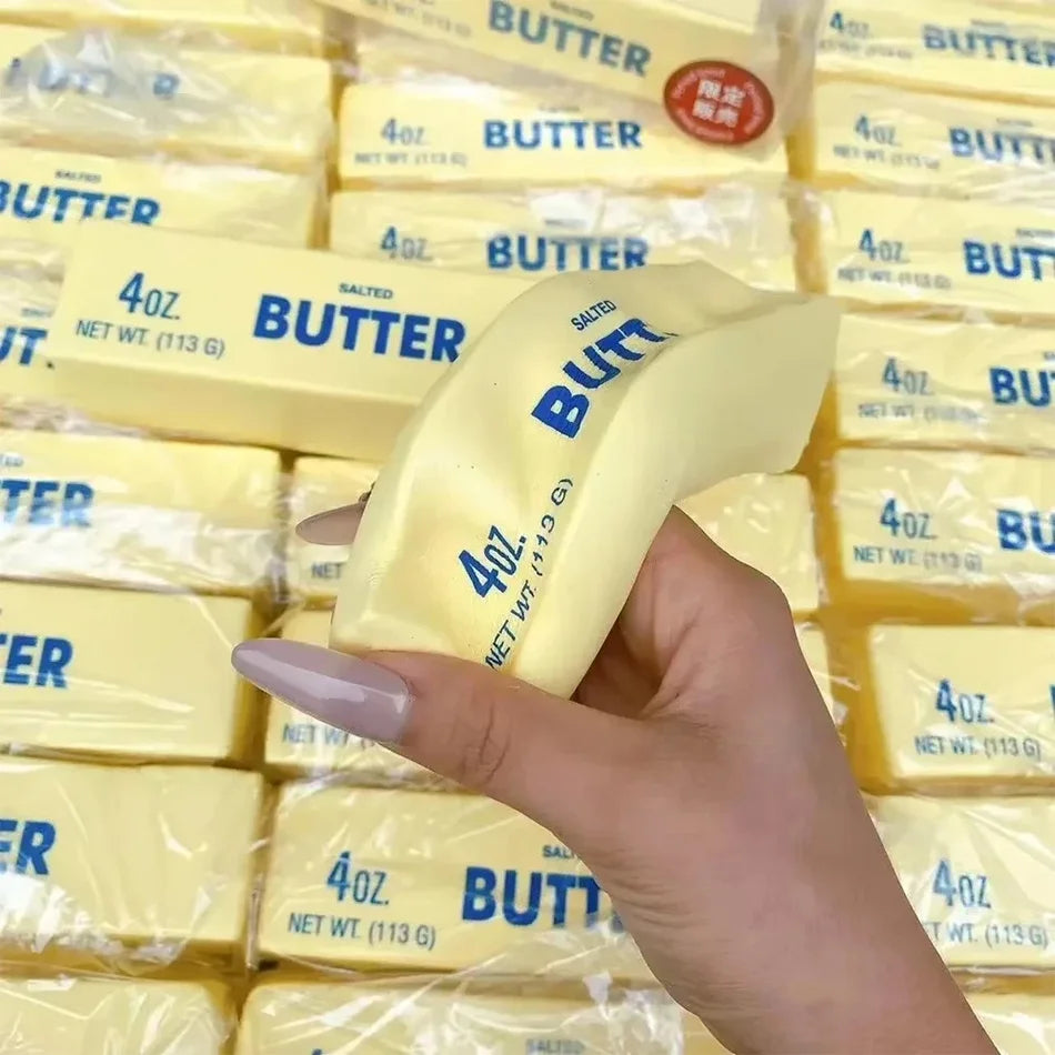 A hand holds a block of yellow butter squishy stress relief toy packaged in clear plastic.