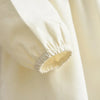 Close-up of a cream or ivory long sleeve dress featuring a gathered bow detail on the cuff.