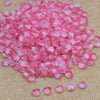 A pile of pink and rose colored tulip flower glass beads scattered on a beige fabric surface.