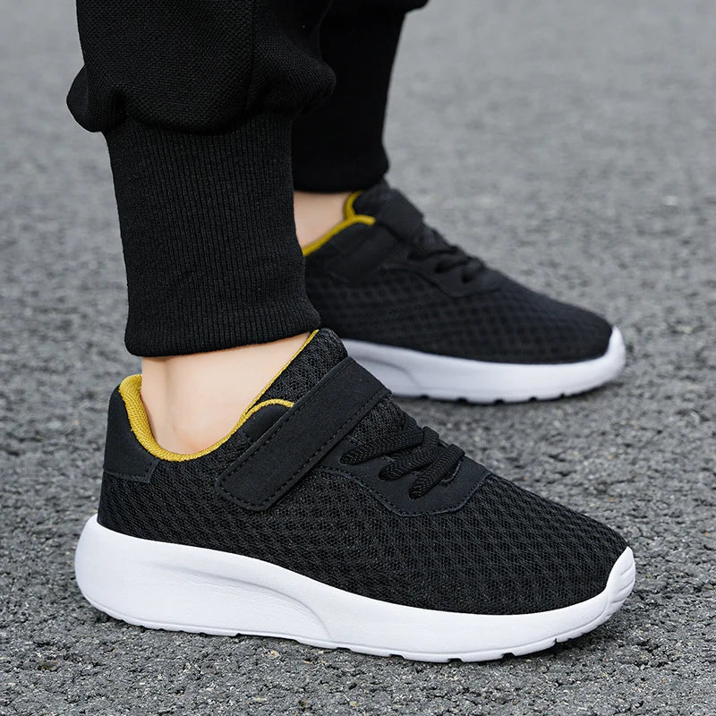 A pair of black and yellow breathable mesh kids' sneakers with hook-and-loop closure resting on a gray surface.
