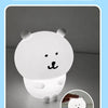 A white silicone lamp shaped like a bear, illuminating a dark background.