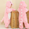 A pink hooded romper resembling a dinosaur is shown on a baby, standing in front of a wooden crib.