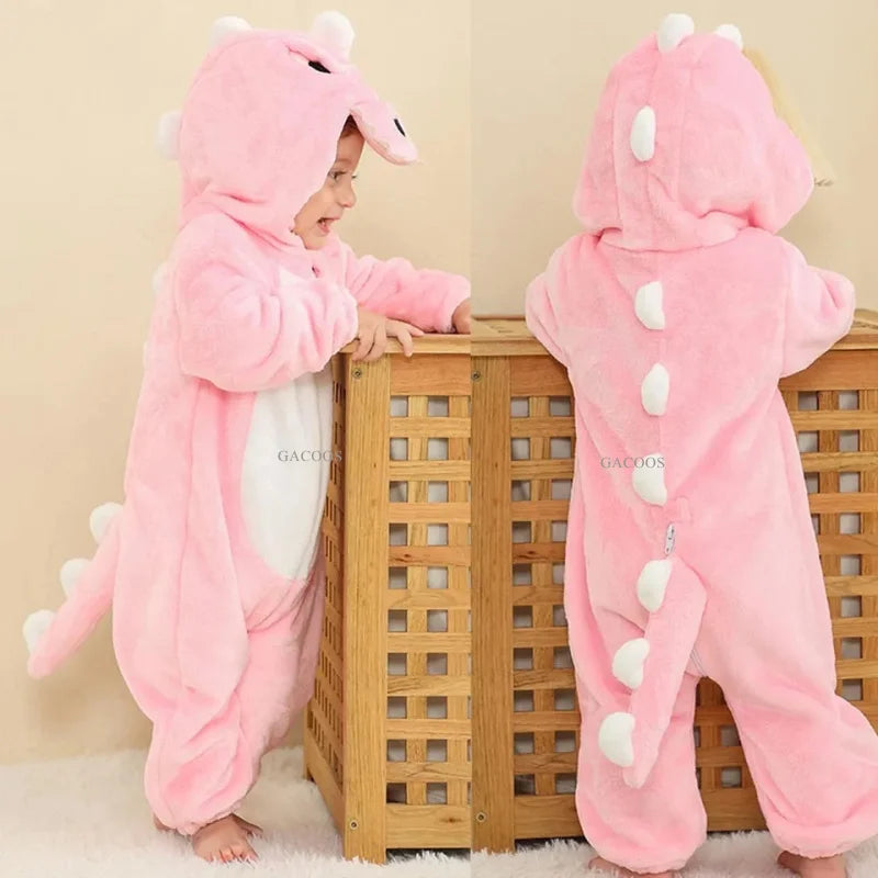 A pink hooded romper resembling a dinosaur is shown on a baby, standing in front of a wooden crib.