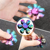 A hand spins a colorful metal fidget spinner with iridescent, translucent blades against a dark background.