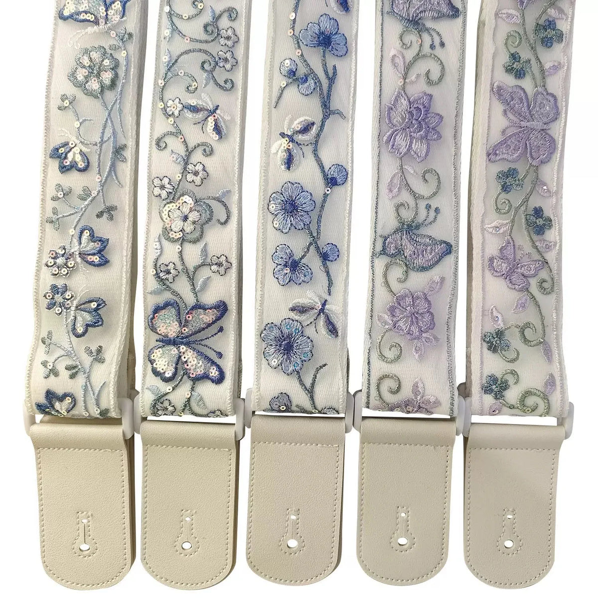 A set of light beige woven guitar straps with floral embroidery and leather accents.
