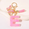 A gold initial E keychain featuring a pink butterfly charm and pink tassel.