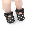 A pair of black bow-knot first walker shoes for a baby girl with a soft anti-slip sole and heart accents.