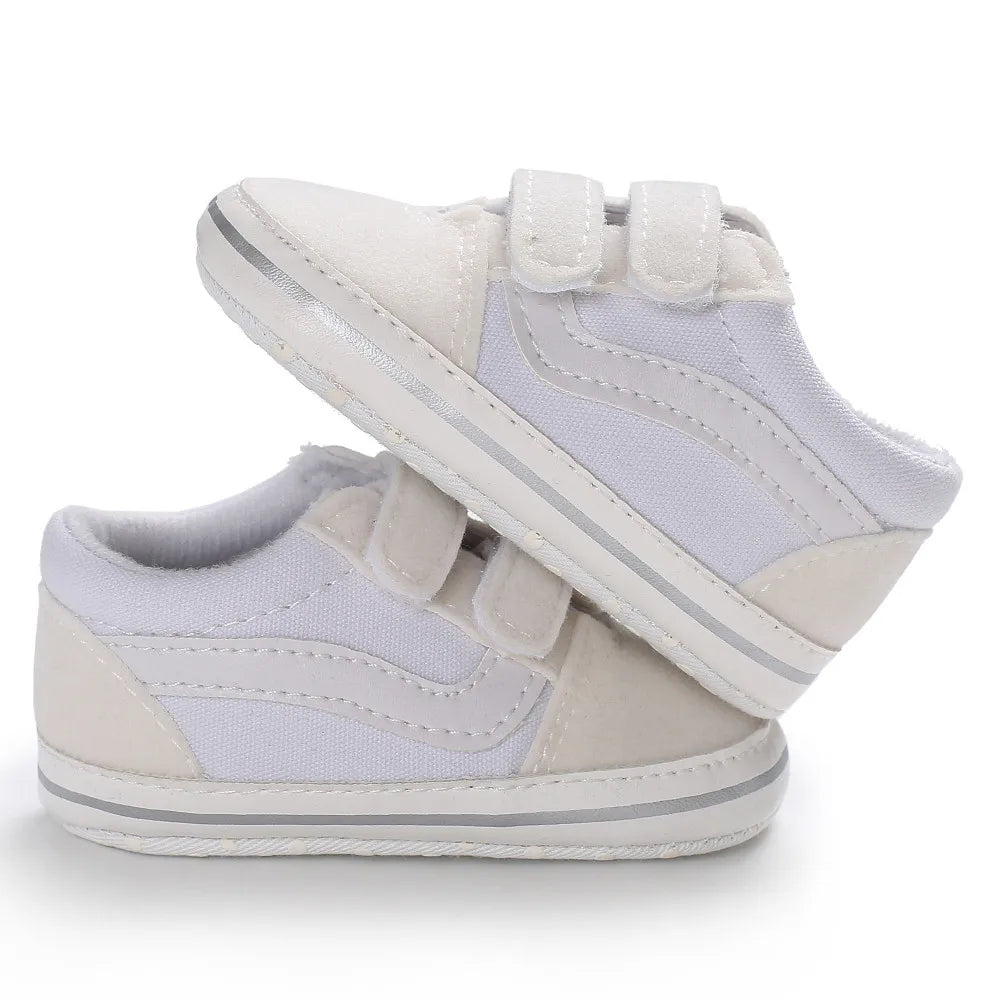 A pair of white canvas baby sneakers with light gray soles and white laces shown from the side.