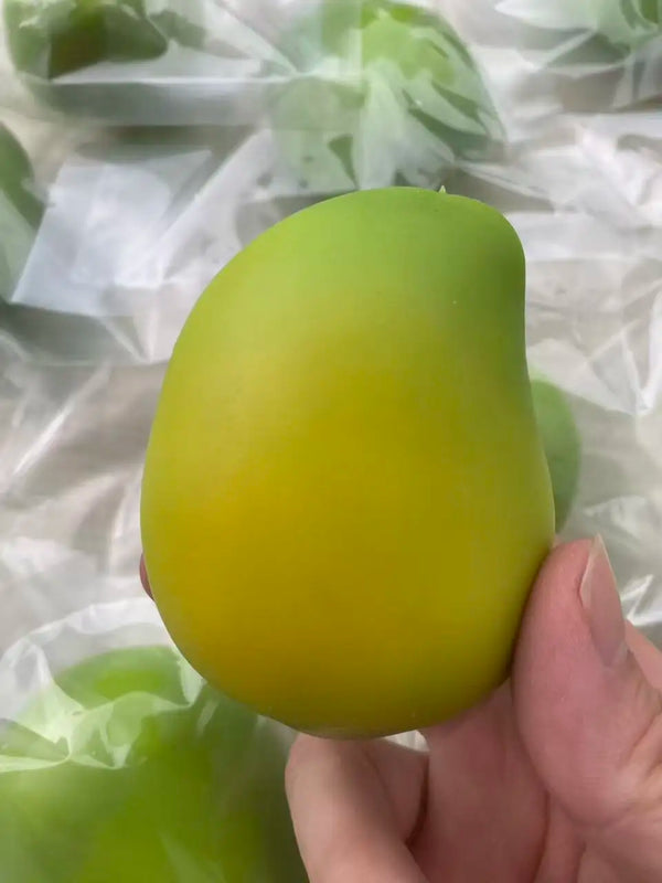 A hand holds a bright yellow, smooth mango-shaped stress ball fidget toy against a translucent background.