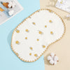 A cream-colored embroidered flat pillow with gold accents rests on a light blue surface.