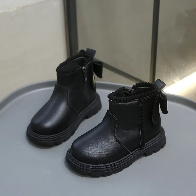 A pair of black faux leather winter boots for kids, shown from the side on a light gray surface.