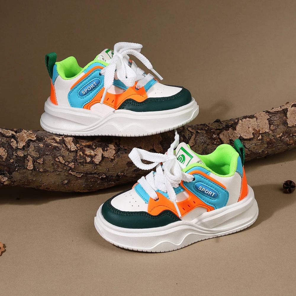A pair of boys' breathable casual sneakers featuring white, teal, orange, and green accents resting on a brown log.