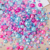 A colorful mix of pink, blue, and purple resin rhinestone pearls with an AB finish scattered on a light wooden surface.