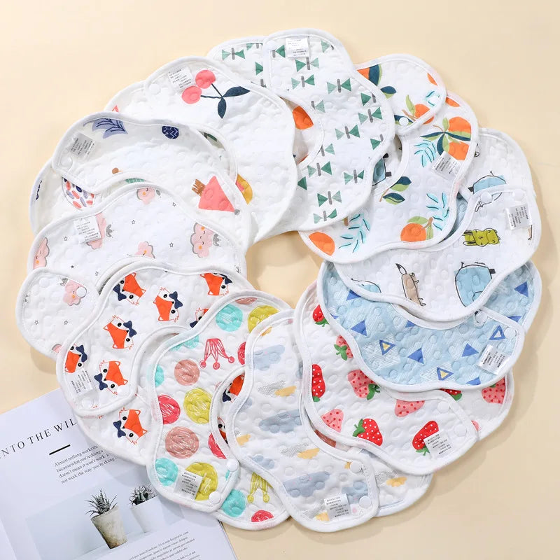 A collection of soft waterproof baby bibs in various patterns and colors laid out on a light background.