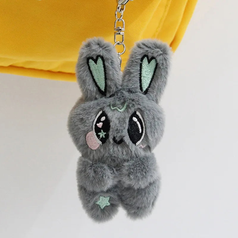 A small, gray plush pendant doll shaped like a rabbit with green accents, hanging from a silver chain.