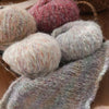 A collection of fluffy, variegated alpaca blend yarn balls in shades of pink, gray, and cream.