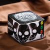 A black box featuring a white Aztec skull design and several smaller skulls, resting on brown fabric.
