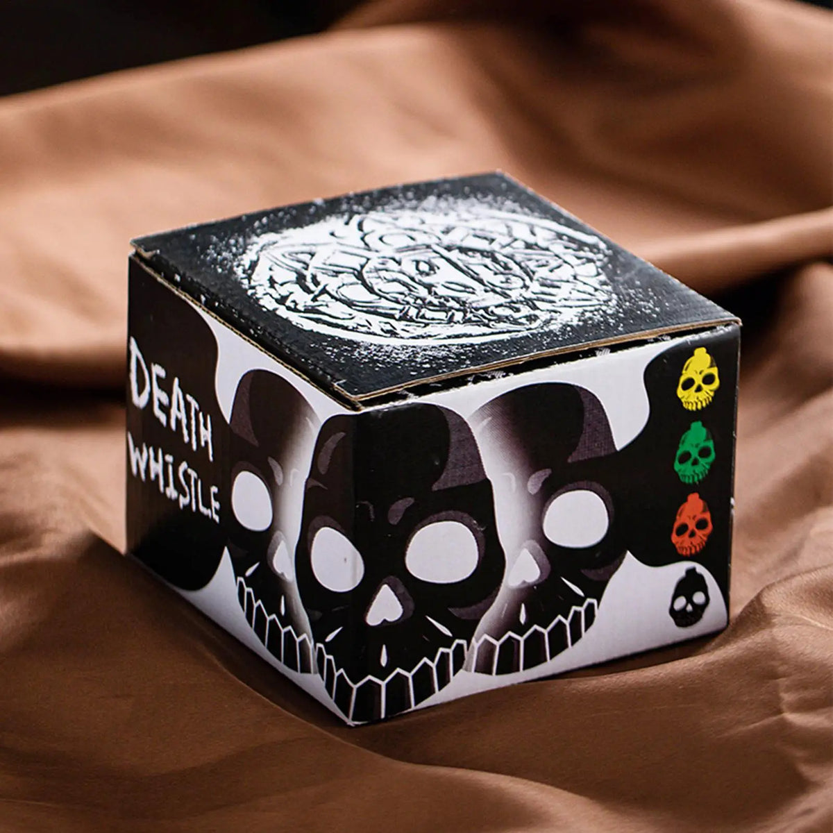 A black box featuring a white Aztec skull design and several smaller skulls, resting on brown fabric.