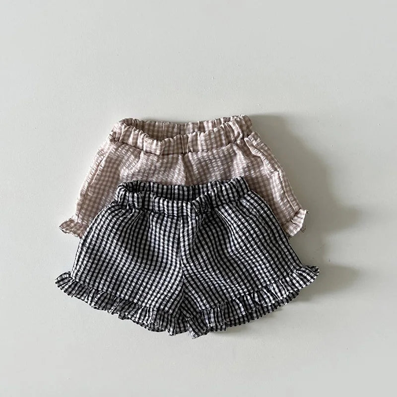 A set of baby girl ruffle top and shorts in checkered patterns, featuring beige and black fabrics.