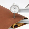A brass caliper measuring 1.8mm leather hide in rust red color against a white background.