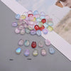A collection of iridescent glass beads in various shades of pink, purple, and blue scattered on a white surface.