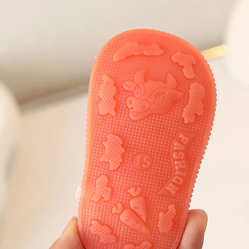 Une sandale d'été antidérapante orange et bruyante pour bébé tenue dans une main.