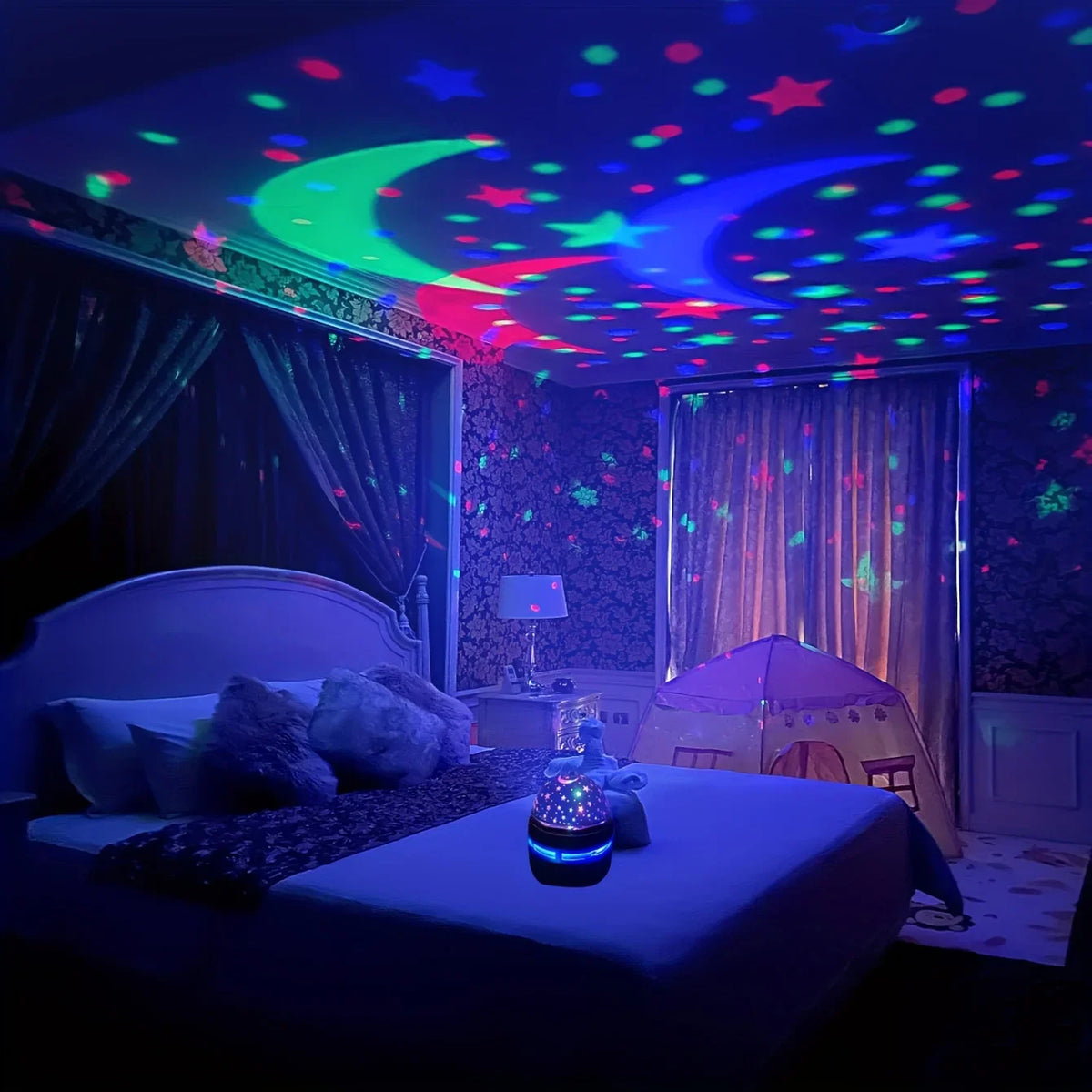 A bedroom scene featuring a galaxy star projector night light with moon and star effects illuminating the ceiling.