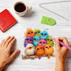 Hands are assembling an animal-shaped acrylic pendant craft kit featuring colorful birds on a wooden base.